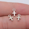 Three silver metal cross charms with hanging rings displayed on a finger for scale - White Gold