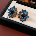 Detail shot of vintage floral stud earrings featuring blue and grey crystals on a pad - Silver Earring Post-Blue