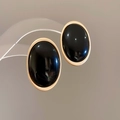 Macro detail van ovale zwarte hars oorbellen met gepolijste goudkleurige frames op houder - Zilveren Naald Ovalen Stijl / Goud-Zwart