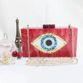 Macro detail of red acrylic evening bag featuring marble texture and devil eye emblem - Red