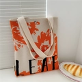 Detail of knitted tote bag with orange leaf pattern and black LEAF lettering on desk - Leaf Orange