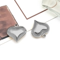 Gros plan de deux pendentifs creux en forme de cœur en acier inoxydable argenté avec anneaux - Coeur Creux (Grand) / Acier