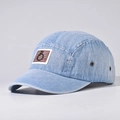 Detail van een lichtblauwe denim 5-panel pet met bruine patch en metalen oogjes - Licht denim