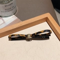 Detail of leopard print bow hair clip with gold metal buckle on a wooden tray - 3D Dark Leopard Bobby Pin