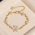 Luxuriöses goldenes Blumenarmband mit Zirkonia-Steinen in einer beigen Schmuckschatulle - Blume Weißer Zirkon Gold