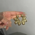 Handgehaltene goldene abstrakte Blumen-Ohrringe mit glänzendem Spiegel-Effekt - Großer Abstrakter Blumen-Goldreif