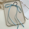 Detail of light blue ribbon hair tie with long tassels on a beige decorative tray - Blue
