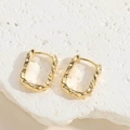 Close-up of golden square hoop earrings with hammered texture on white stone surface - Hammered U-Shape