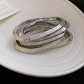Macro detail of silver layered metal bracelet with ribbed texture on white ceramic tray - Silver