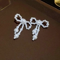 Details von eleganten Schleifen-Ohrringen mit langen Perlen-Quasten auf Lederhintergrund - Goldene Schleifen-Perlenohrstecker mit Silberstift