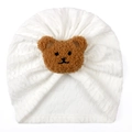 Detail view of white knitted baby turban hat with a cute brown plush bear ornament - One Size / White