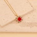 Vue détaillée d'un collier doré vintage avec pierre rouge et accents verts sur marbre - Rouge