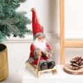 Christmas Santa Claus doll on a wooden sleigh for festive holiday tabletop decoration - Red