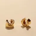 Detalle de pendientes de aro dorados retorcidos con textura metálica pulida y brillo elegante - Dorado