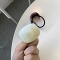 Elastic hair tie with a large cream resin bead shown in a close-up handheld shot - White Texture