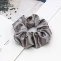Close-up of a grey satin scrunchie with smooth silk texture on minimalist magazine - Silver