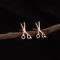 Detailed close-up of rose gold scissors earrings on a rustic wood branch against black background - Rose Gold
