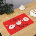 Close-up view of a red linen Christmas placemat with Santa Claus motifs and Merry Christmas text - Three Gnomes Style