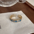 Nahaufnahme des Goldrings mit blau-grauem Emaille-Karomuster auf beigem Stoff - Einstellbar Offen / Blauer Feingitter-Emaille-Stil