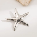 Silver starfish brooch with hammered metal texture displayed on a natural stone base - Starfish Steel