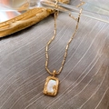 Detalle de cadena chapada en oro con colgante rectangular de nácar sobre fondo gris - Collar-Estilo Nácar Rectangular / Dorado