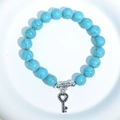 Blue turquoise beaded bracelet with a silver heart-shaped key pendant on white plate - Blue Turquoise Heart Key Charm