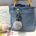 Detail of soft grey plush ball pendant with purple star clip hanging on a denim handbag - Gray