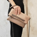 Beigefarbene Leder-Clutch mit Metallnieten und Kettenriemen wird in der Hand gehalten - Khaki