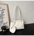 Detail of cream white faux leather tote bag with heart charm on a black desk set - White
