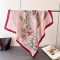 Detail of silk scarf with pink floral peony print and red rolled edges on a metal rack - Red