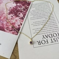 Detail of gold necklace with a round purple gemstone pendant and white diamond halo - February Dark Purple
