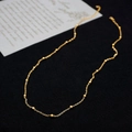 Minimalistische goldene Titanstahl-Perlenkette auf einer strukturierten schwarzen Fläche - 60cm Halskette
