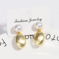 Macro detail of gold brushed metal drop earrings with white pearls on a display card - Gold