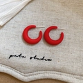 Detail of matte red C-shaped acrylic earrings with silver needles on a textured fabric - Red C-Shape