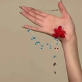Détail d'un collier artisanal avec fleur en tissu rouge et perles bleues tenu à la main - Bleu-Rouge-Fleur