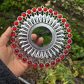 Detailed close-up of a silver sunburst wall decor with a red gemstone center held by hand - Bright Silver Red