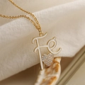 Golden necklace with Fe letter pendant and sparkling rhinestone heart on beige fabric - White