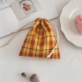 Detail of yellow checkered drawstring pouch used as a cosmetic bag on a white desk - Bubble Orange-Yellow Grid
