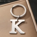 Silver metal letter K keychain with round ring displayed on a brown gift box cover - Letter K