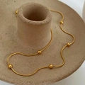 Detail of 18K gold snake bone chain with small metal beads on ceramic display stand - Gold Round Snake Chain + Positioning Beads
