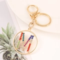 Close-up of golden letter M keychain pendant with multi-colored crystals on a tray - M