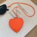 Detalle de colgante de corazón en cuero naranja con textura litchi sobre libro - Naranja