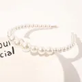 Detail view of white gradient pearl headband placed on a decorative ceramic plate - Three Medium Pearls