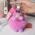 Detail eines rosa Fuchsfell-Bommel-Schlüsselanhängers mit schlafender Babypuppe - Taro-Lila
