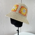 Detail of handmade crochet straw bucket hat with colorful flower patterns on a stand - Beige