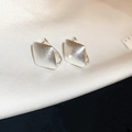 Primer plano de pendientes plateados en forma de U con metal cepillado sobre seda blanca - Ear Cuff De Rombo Cepillado / Plateado