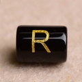 Macro shot of a polished black round bead featuring a gold-stamped letter R for jewelry - Letter R