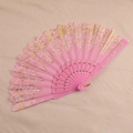 Close-up of pink lace folding fan with ornate gold floral patterns and carved plastic ribs - Pink