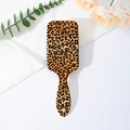 Detailed view of leopard print paddle hairbrush on elegant white fabric with floral decor - Classic Brown Leopard