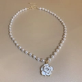 Detail van elegante parelketting met witte emaille camelia bloem en goudkleur - Gouden Bloemen Ketting